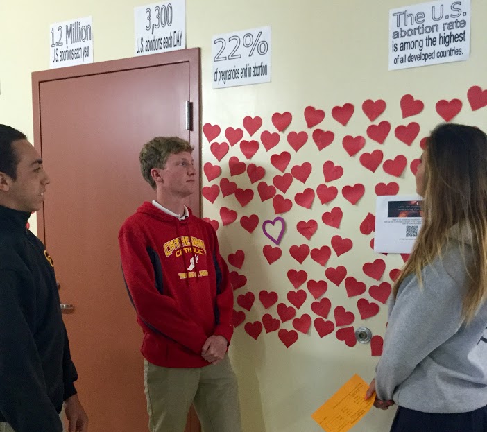 CCHS students JP Sperrazzo ‘17, Michael Robinson ‘17, and Delara Bahadoori ‘18 ponder the deeper meaning behind the hearts that wrap around the De Sales building. The hearts, which are posted by Ms. Christine LaPortes classes, represent aborted children in the U.S.
