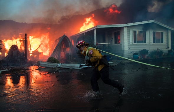 A fireman from the Oceanside Fire Department bravely rushes to the scene of the Lilac Fire, hose in hand, in an attempt to save the surrounding houses from damage. 