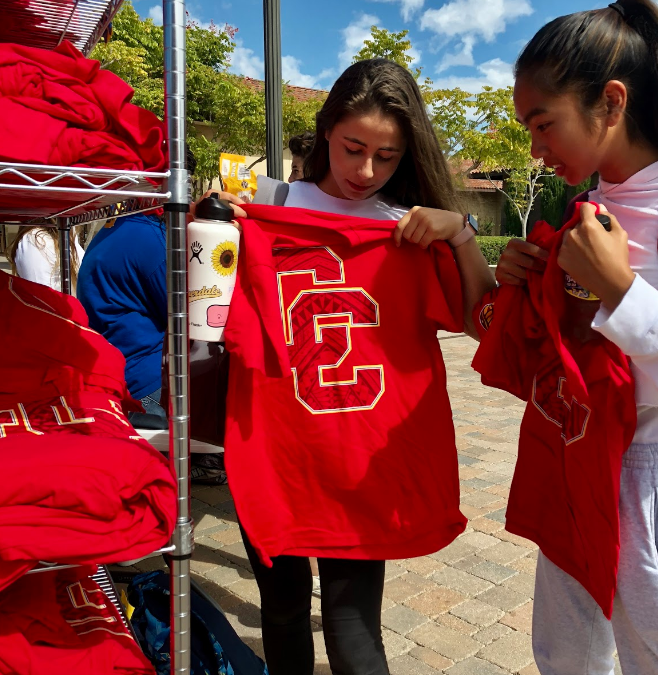 Victoria Jorge ‘22 and Julia Cariquitan ‘22 select “It takes a village to Raise a Don” shirts in preparation for Cathedral Catholic High School’s varsity football “red-out” homecoming game on Friday.
