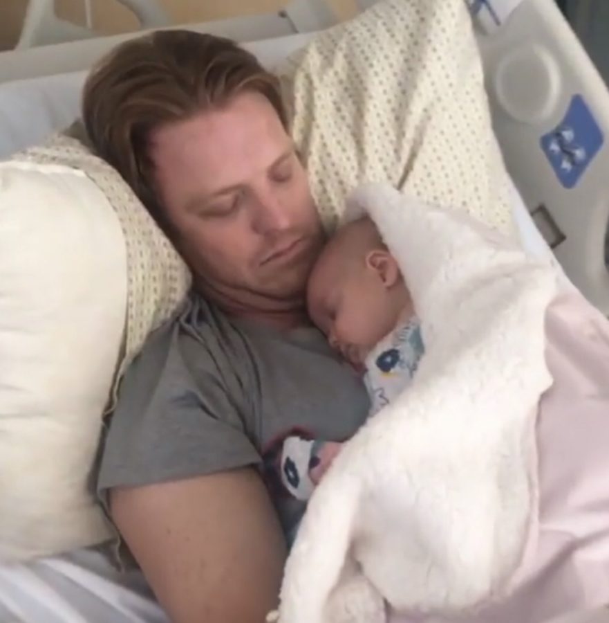 Mr. Chase Tucker lies in a hospital bed with his two-month old daughter, Kennedy Tucker, before his craniotomy.
