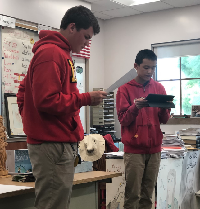Max Miller ‘21 assists Michael Wang ‘21, a Torrey Pines High School transfer student, during his saint presentation last Thursday, which took place in Mr. Phil Remington’s classroom. 
