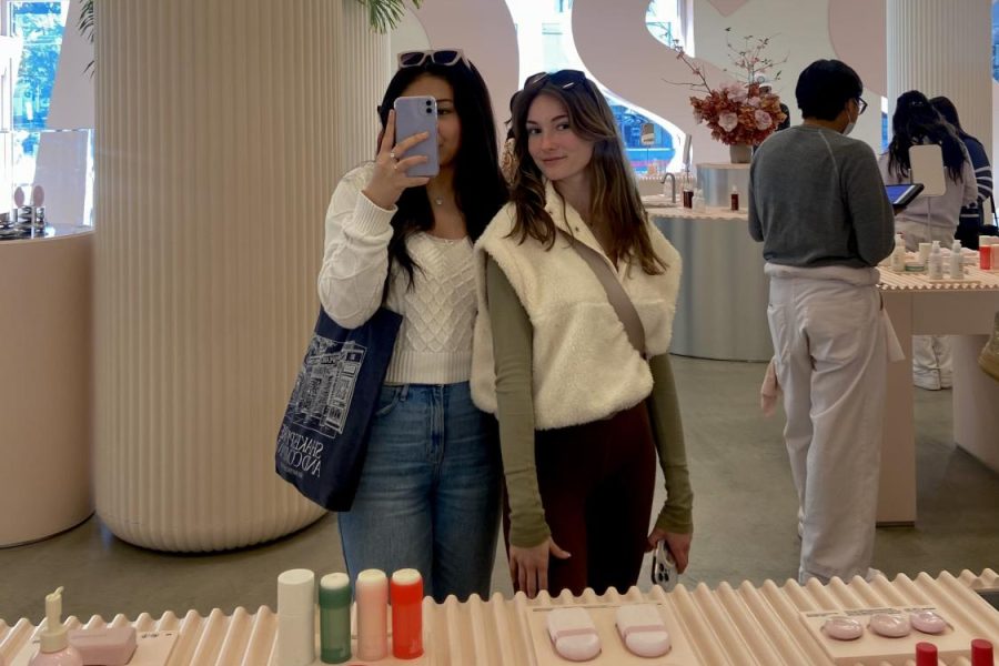 Former and current Cathedral student shopping in store at Glossier Los Angeles. Products pictured: Body Hero Exfoliating Bar, Deodorant, Hand Cream, Glossier You Solid, Body Hero Daily Oil Wash, Glossier Candles, Glossier You (Left to right, top to bottom).
