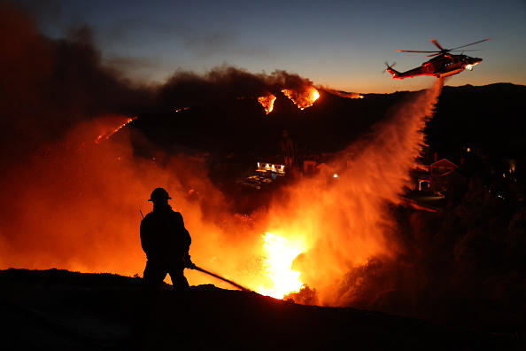 TOPSHOT - Fire personnel respond to homes destroyed while a helicopter drops water as the Palisades Fire grows in Pacific Palisades, California on January 7, 2025. Terrified residents caught in blazing neighbourhoods, influencers ignoring the ban on drones and the frightening unpredictability of the wildfires are just some of what journalists covering the fires ravaging Los Angeles for AFP have had to manage.

The United States' second-largest city has never faced a blaze of this scale, driven by an extreme autumn drought and fierce Santa Ana winds -- the strongest since 2011 -- that have turned dry hills into kindling, fuelling a relentless inferno that has raged for more than a week. 

Photo by David Swanson / AFP via Getty Images