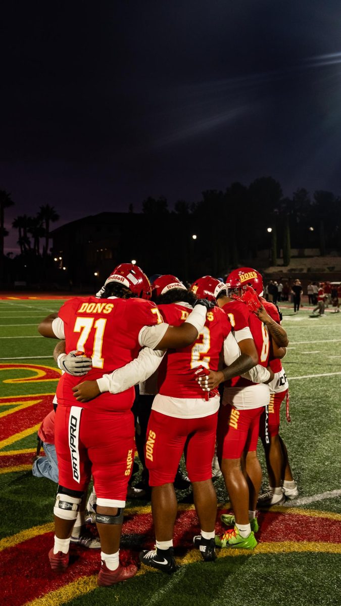 Players gather in the middle of the field to pray with heads bowed and arms wrapped around each other.